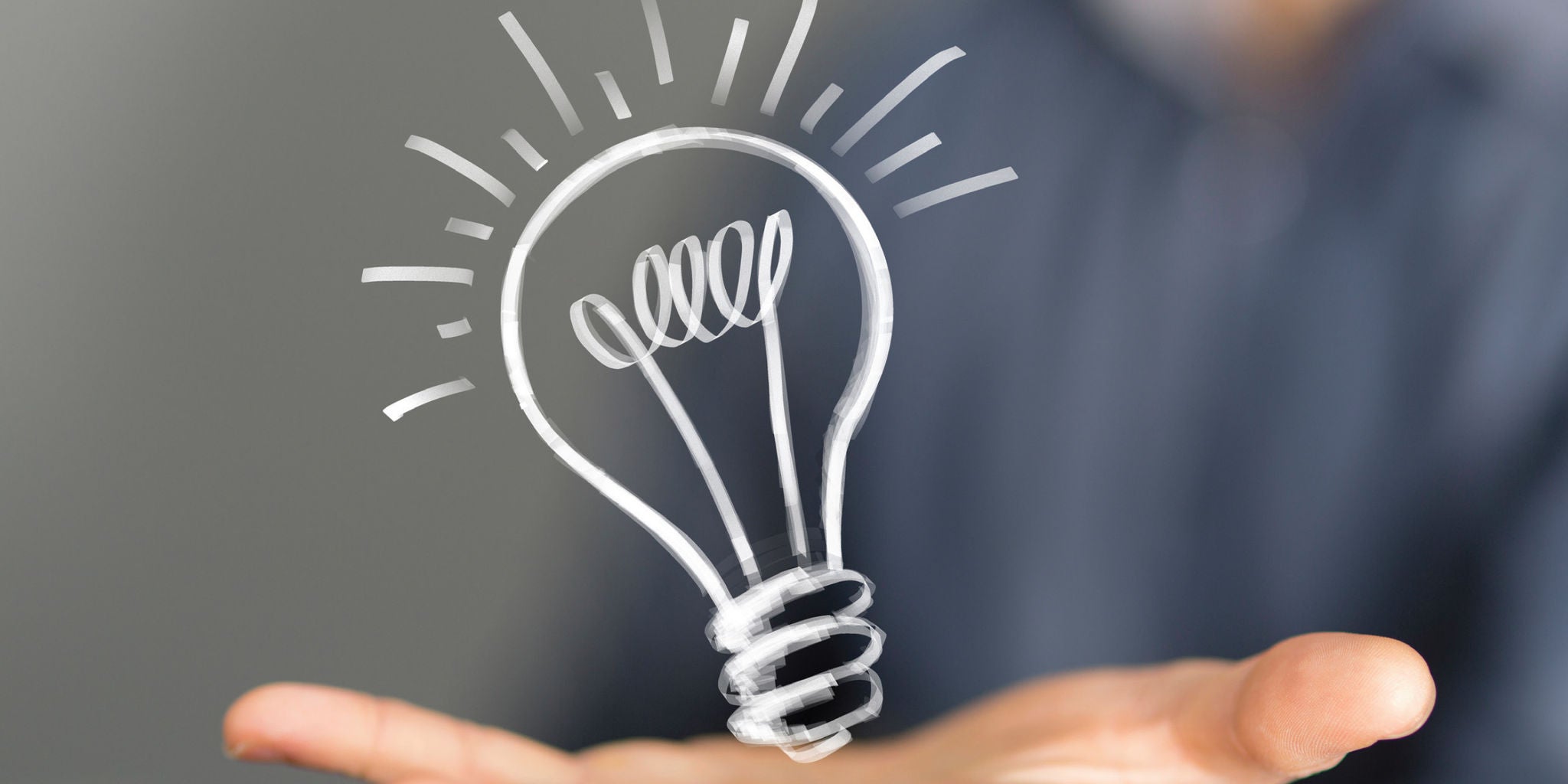 A person extends their open hand forward, with a digitally drawn light bulb hovering above the palm. The light bulb illustration features glowing lines, symbolizing a bright idea or innovation. The background is softly blurred, focusing attention on the hand and the creative concept. The overall mood is inspirational and modern.