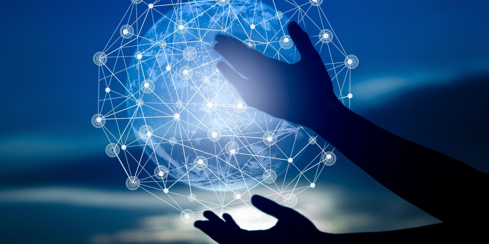A pair of silhouetted hands appears to interact with a glowing, interconnected digital sphere composed of network lines and nodes. The background features a gradient blue sky, creating a futuristic and technological atmosphere. The image conveys themes of innovation, connectivity, and digital transformation. No visible text or numbers are present.