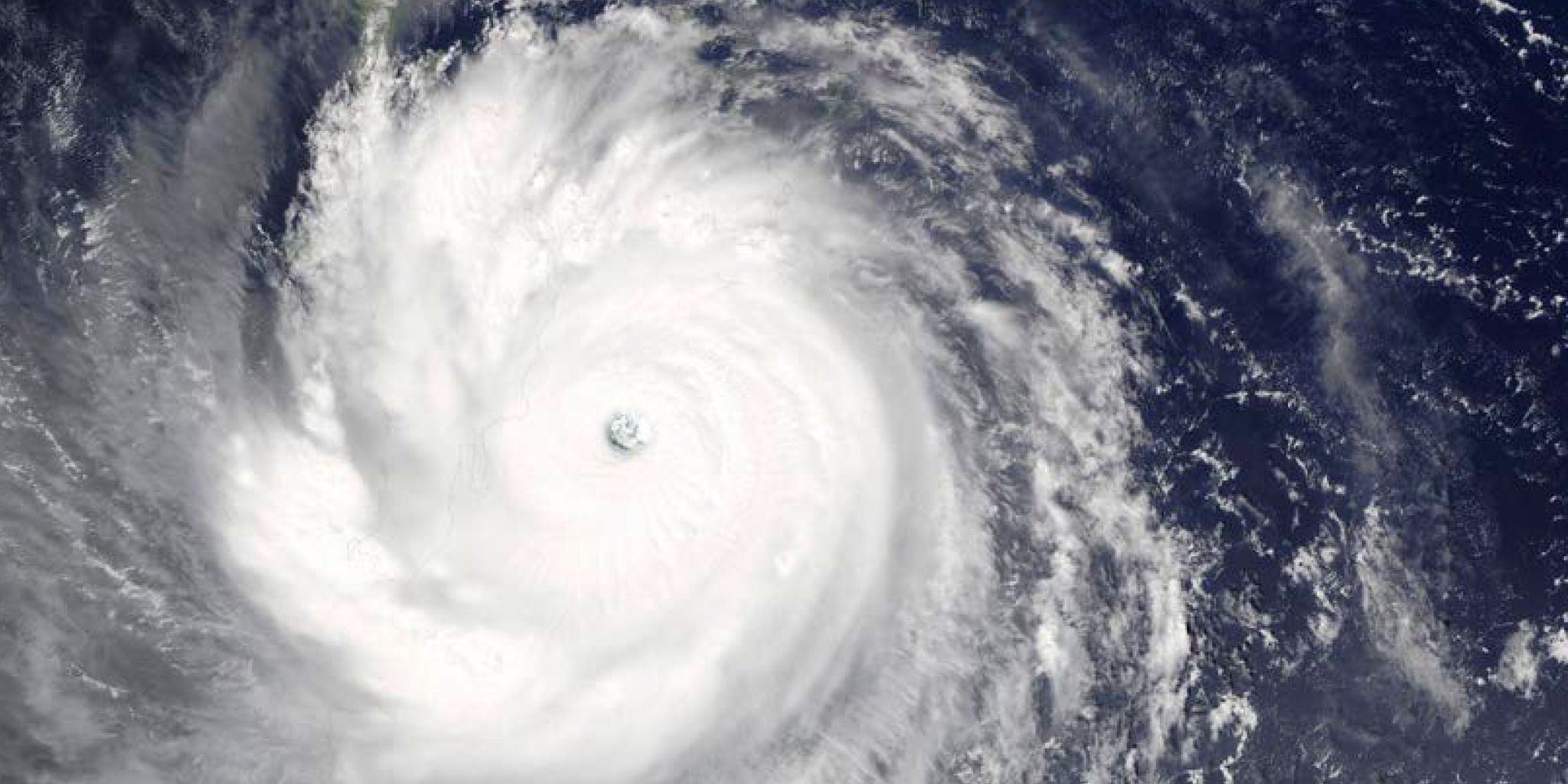 A dramatic satellite image captures a powerful hurricane forming over the deep blue ocean. The swirling cloud bands and distinct eye of the storm are clearly visible, highlighting the storm's intensity. The image provides a striking visual of natural weather phenomena from a high-altitude perspective. No visible text or numbers are present.