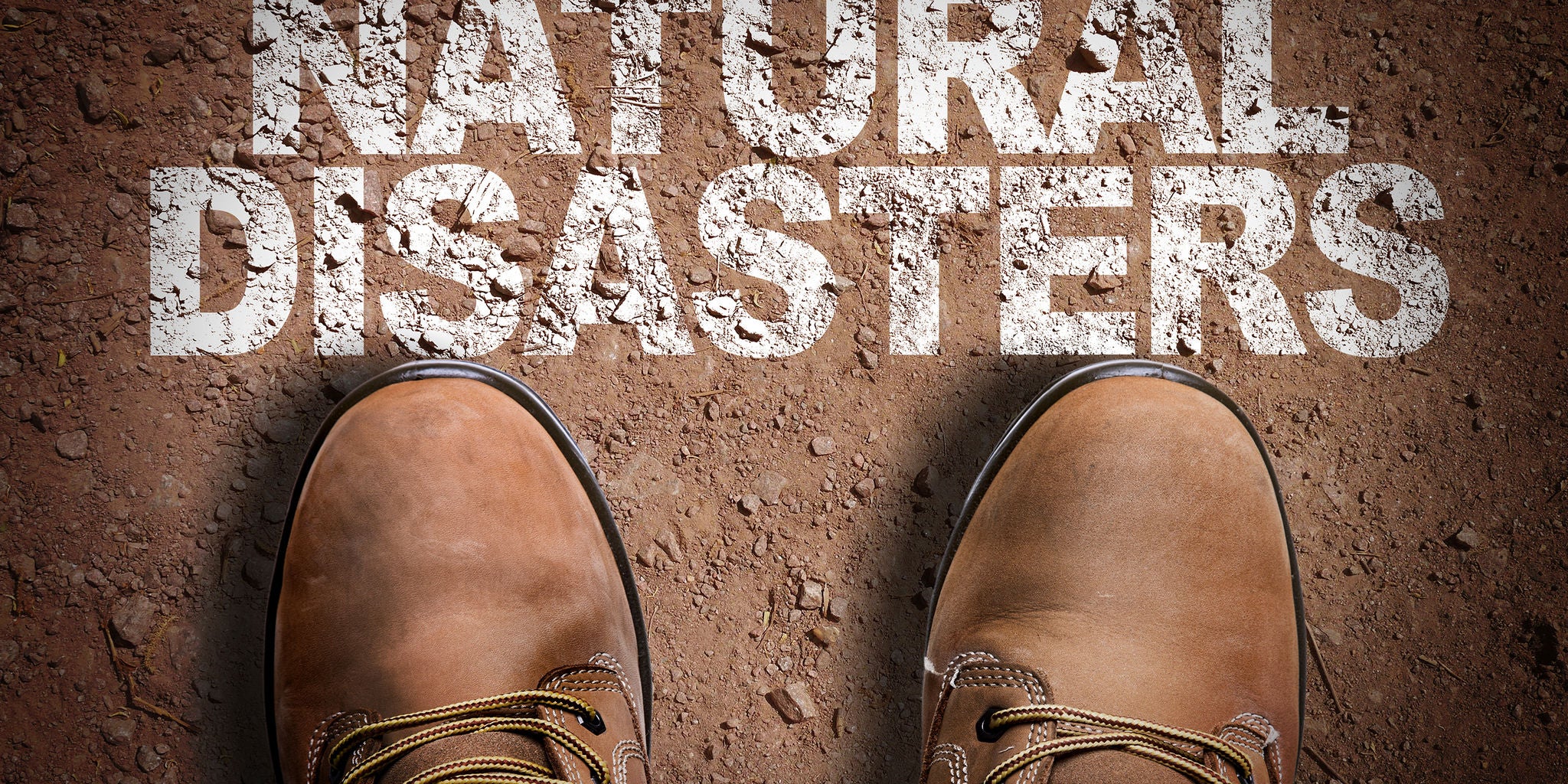 A pair of brown work boots stands on a dirt surface, viewed from above. The words 'NATURAL DISASTERS' are clearly visible in large, bold white letters on the ground. The image evokes a sense of preparedness or response to emergency situations. The earthy tones and rugged footwear suggest outdoor or disaster-related activity.