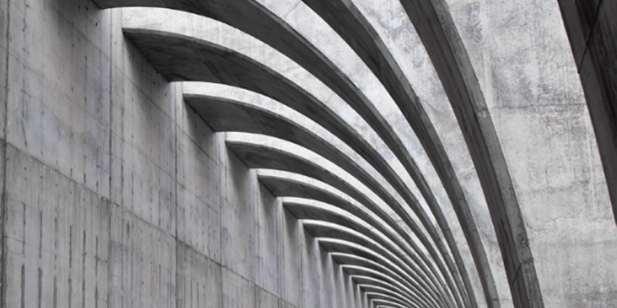 A striking architectural design featuring curved concrete beams in a repetitive pattern. The structure showcases modern industrial aesthetics with clean lines and a monochromatic palette. The setting emphasizes symmetry and depth, creating a visually captivating perspective.