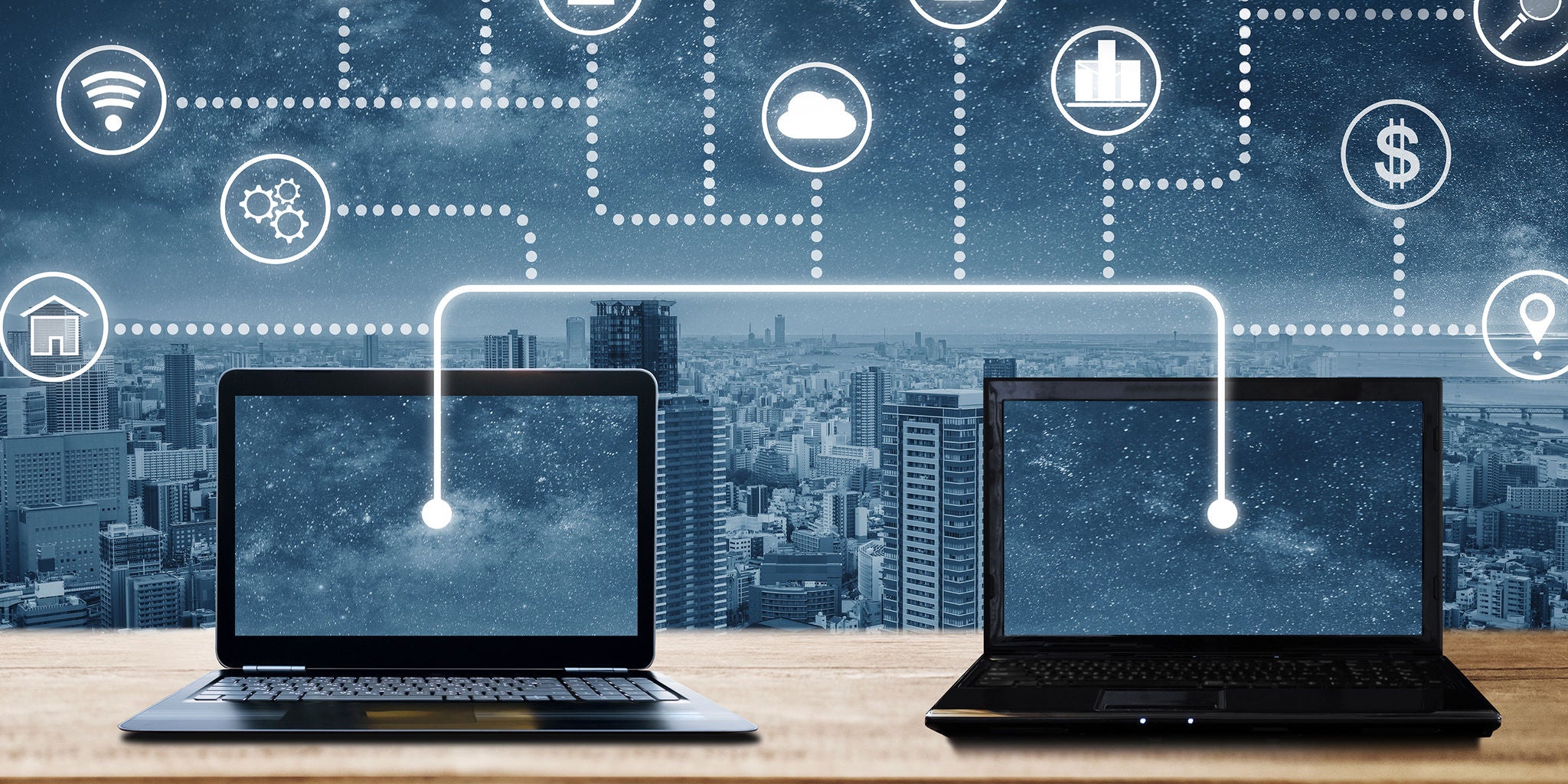 Two laptops are positioned on a wooden surface with a cityscape in the background. Digital network icons and dotted lines connect the laptops, symbolizing data transfer or cloud computing. The scene features a modern, technological atmosphere with a blue and black color palette. No visible text or numeric values are present in the image.
