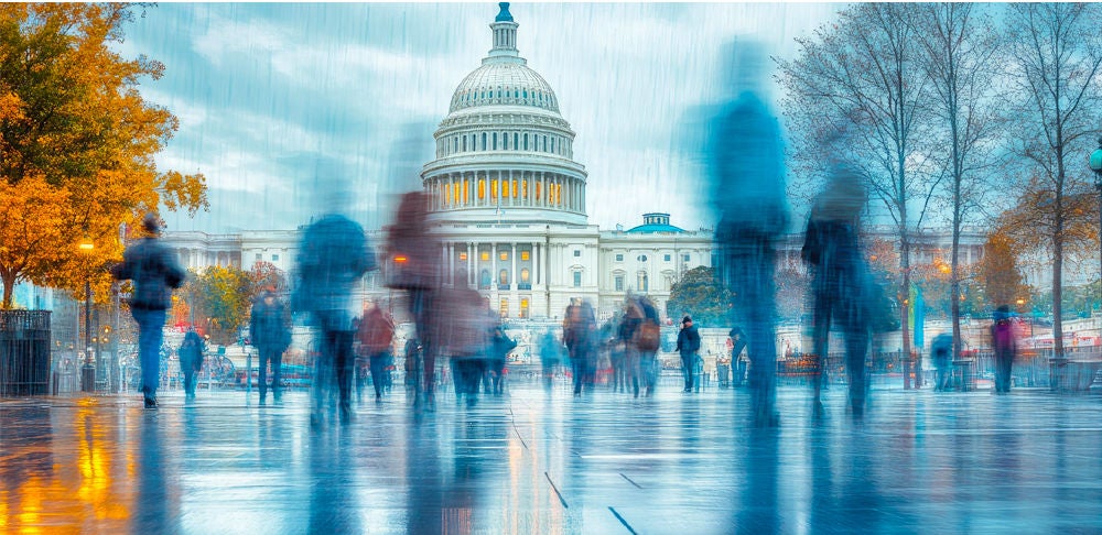 Blurred pedestrians walk across a rain-slick plaza in front of the U.S. Capitol building